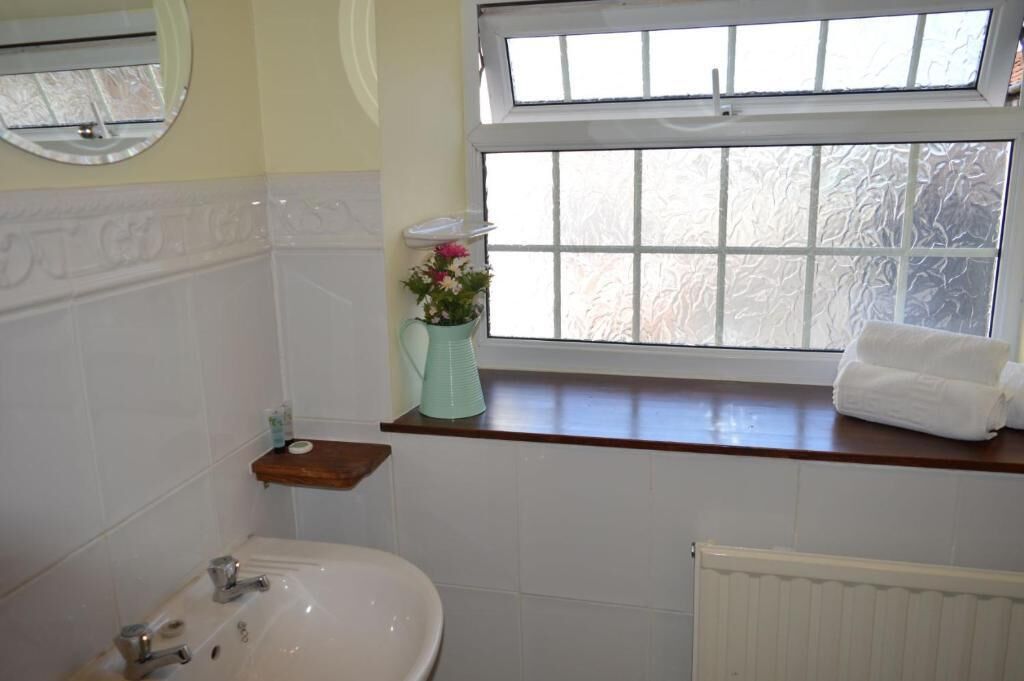 Un baño con un lavabo blanco, un espejo, una ventana con vidrio esmerilado y una toalla en el alféizar.