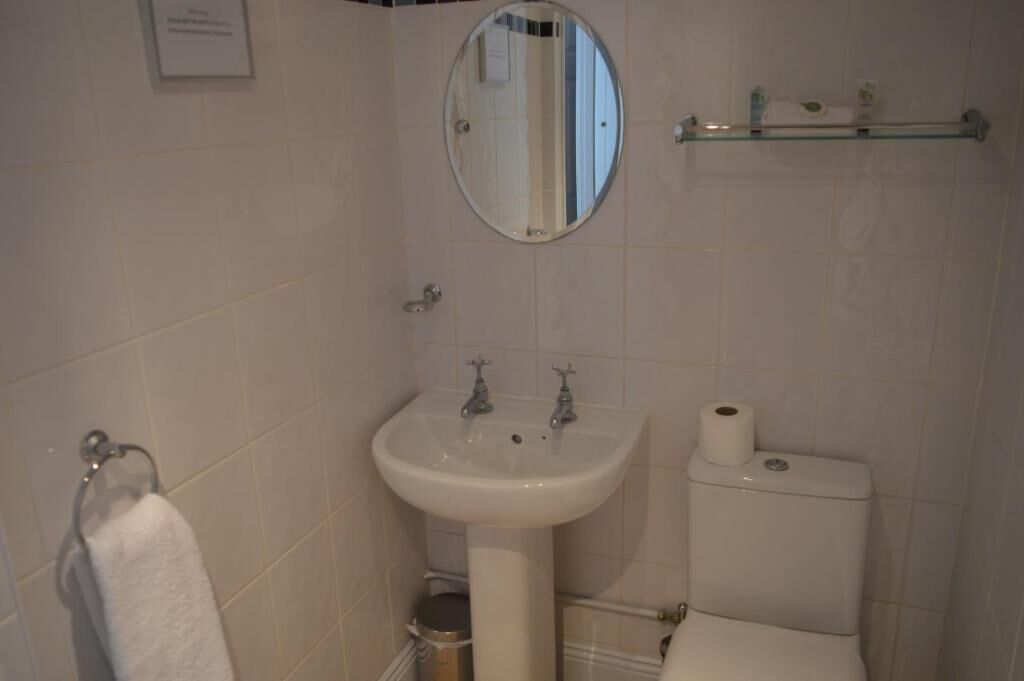 Ein Badezimmer mit einem weißen Waschbecken, einem Spiegel, einer Toilette und einem Handtuchhalter.