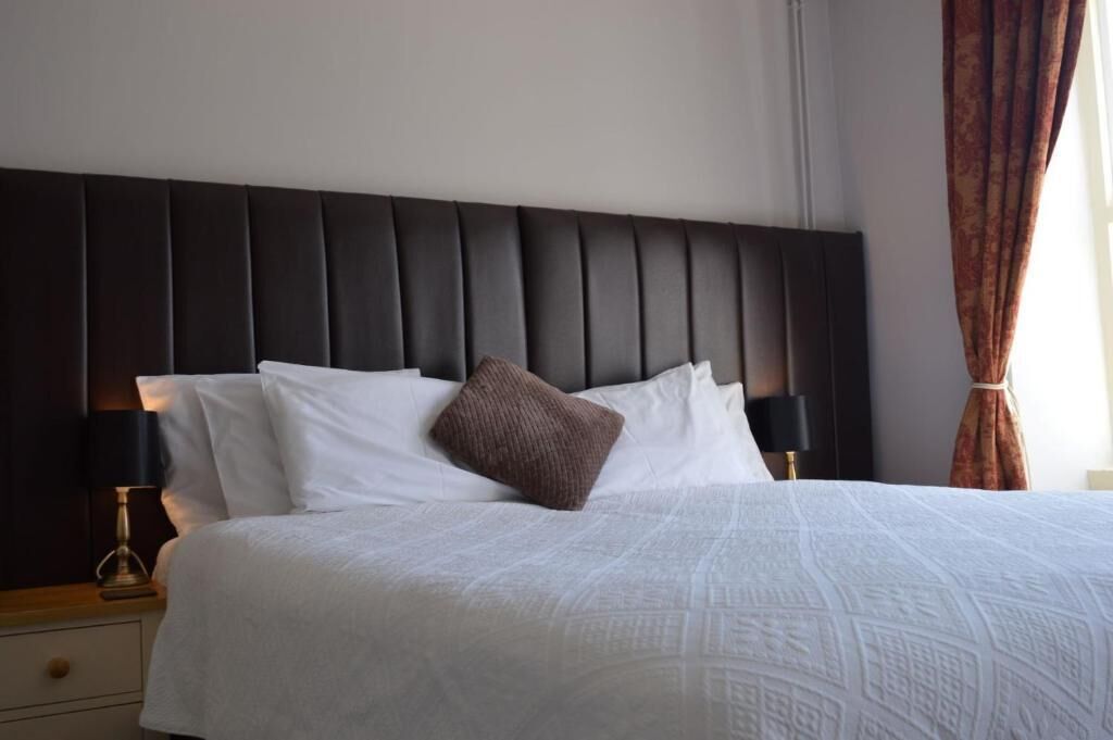 A neatly made bed with a dark headboard, white bedding, and a single brown pillow.