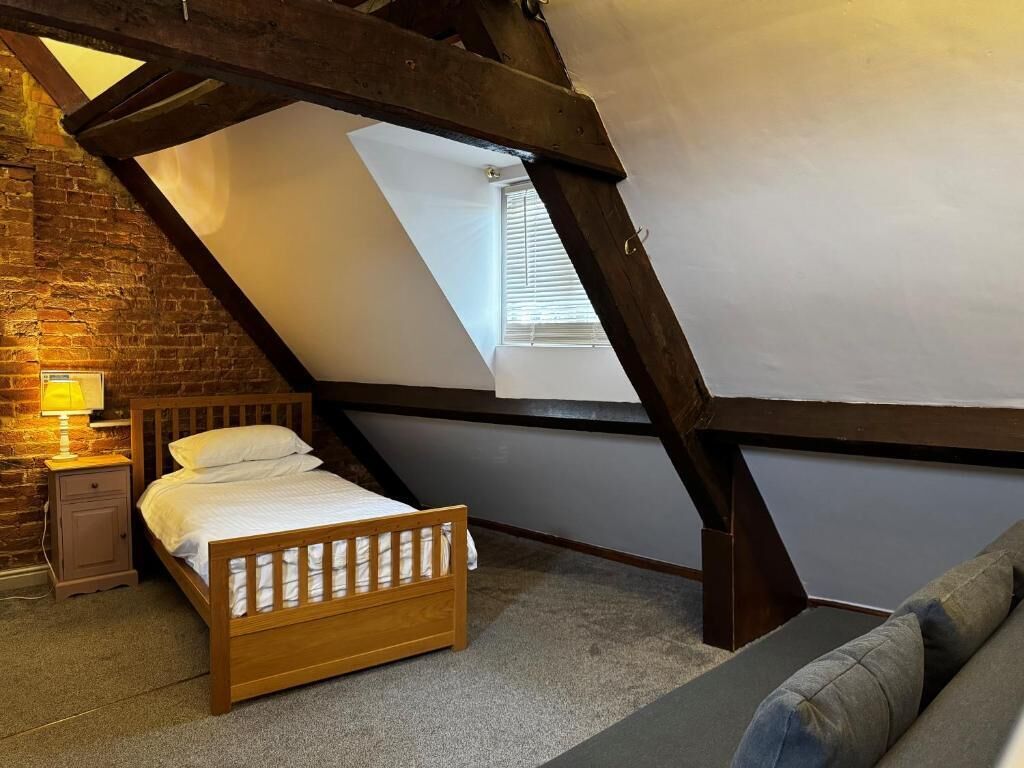 An attic bedroom with a sloped ceiling, a wooden bed, a nightstand, a lamp, and a view through a skylight.