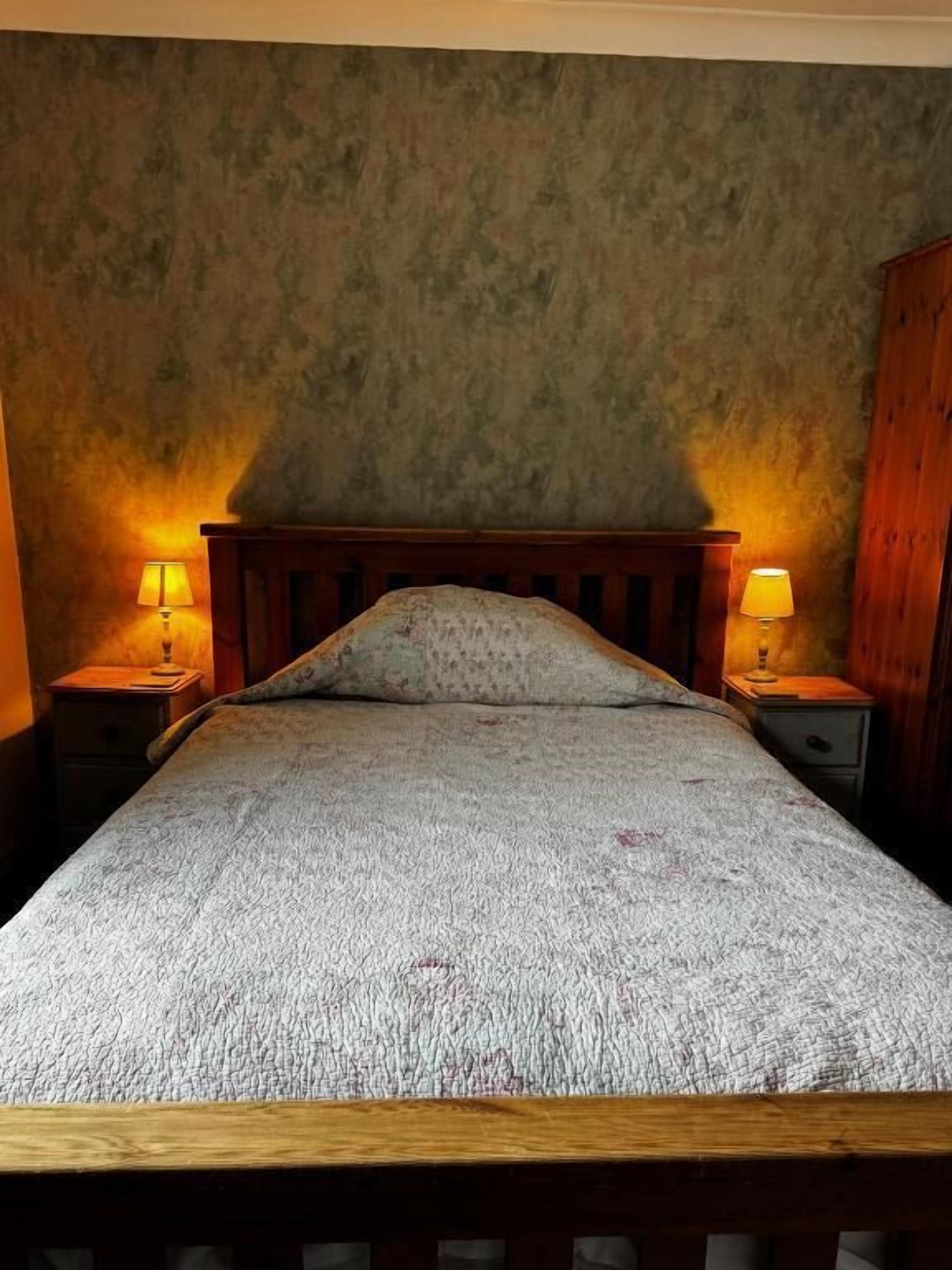 A bed with a wooden headboard, two bedside tables with lamps, and a textured wall.