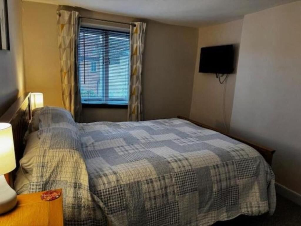Quarto com cama, cortinas, televisão na parede e janela com persianas.