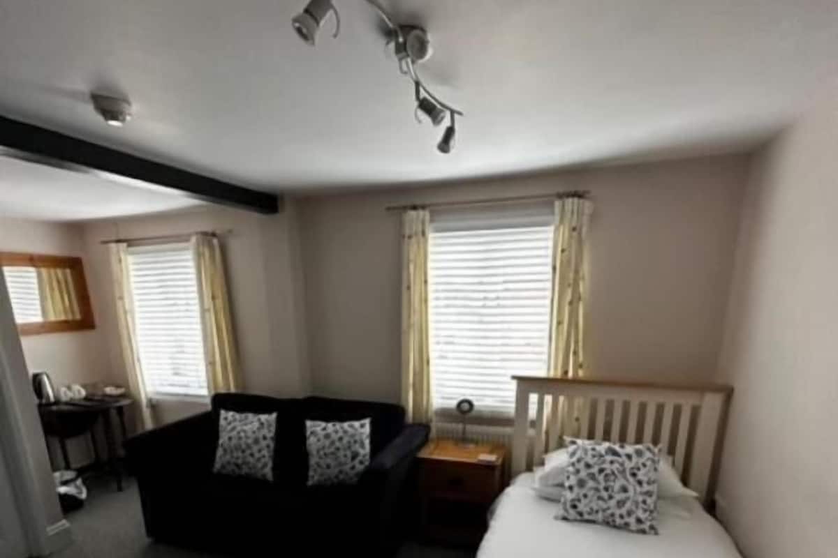 Una habitación con cama, sofá, escritorio y ventana con cortinas.