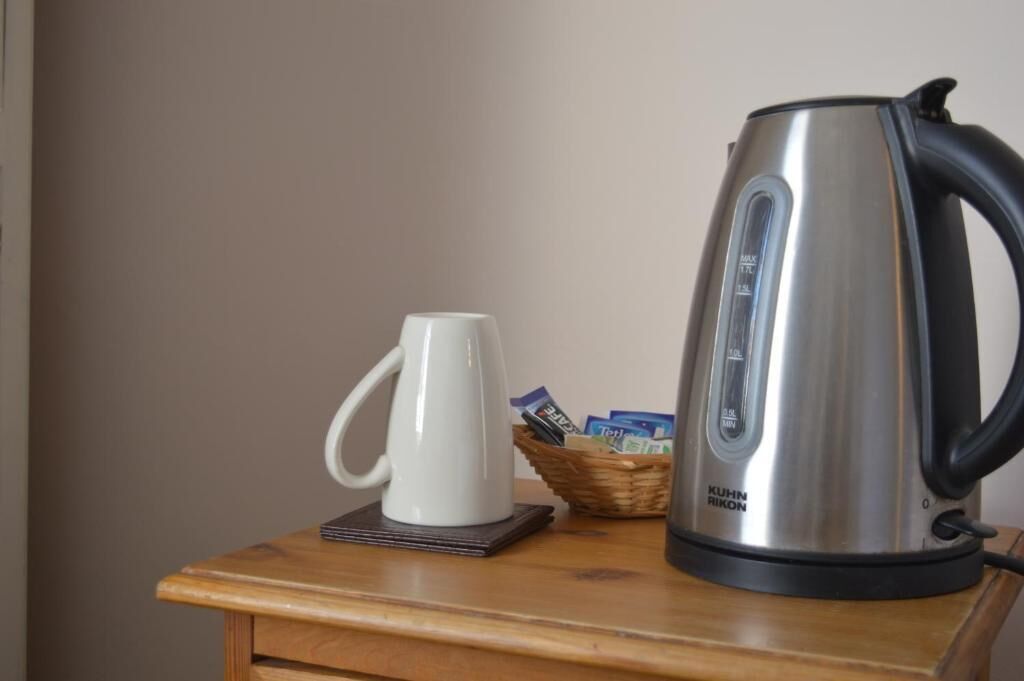 A stainless steel kettle, a white mug, and a basket with items on a wooden table.
