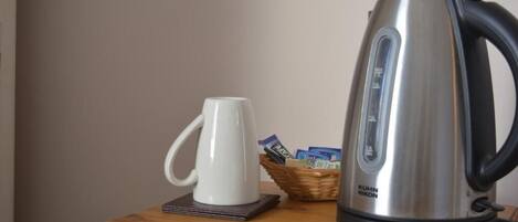 A stainless steel kettle, a white mug, and a basket with items on a wooden table.