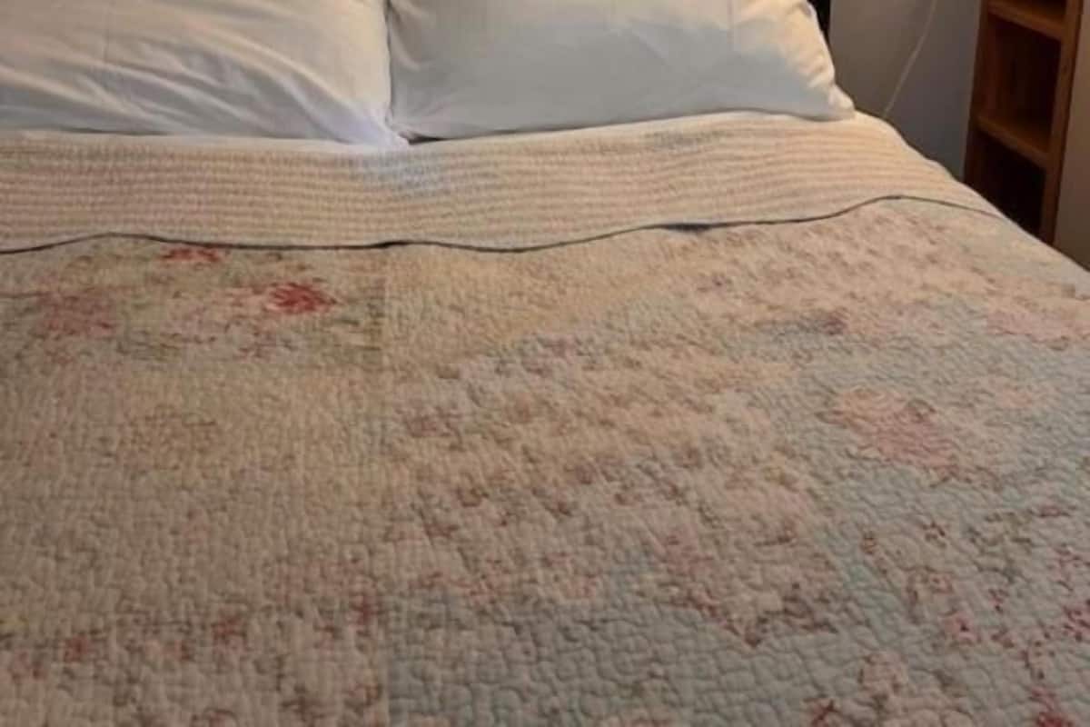 Una cama con ropa de cama blanca, un cuadro en la pared y una lámpara de noche.