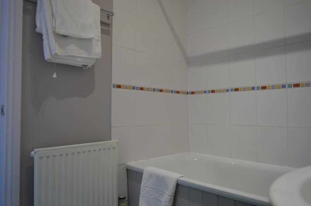 A bathroom with a bathtub, white tiles, a radiator, and a towel rack.