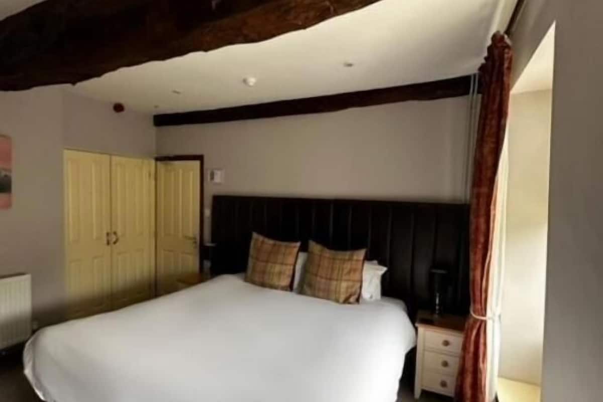 Un dormitorio con una cama grande, vigas de madera, un armario y una ventana.