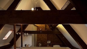 Een slaapkamer op zolder met een schuine kap, een bed met bloemenbeddengoed, twee nachtlampjes en een spiegel boven het bed.