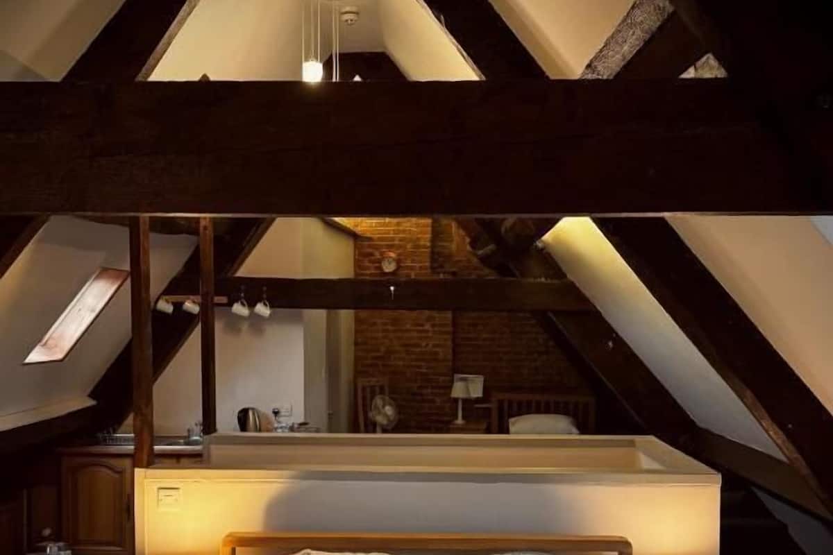 Un dormitorio en el ático con techo inclinado, una cama con ropa de cama floral, dos lámparas de noche y un espejo sobre la cama.