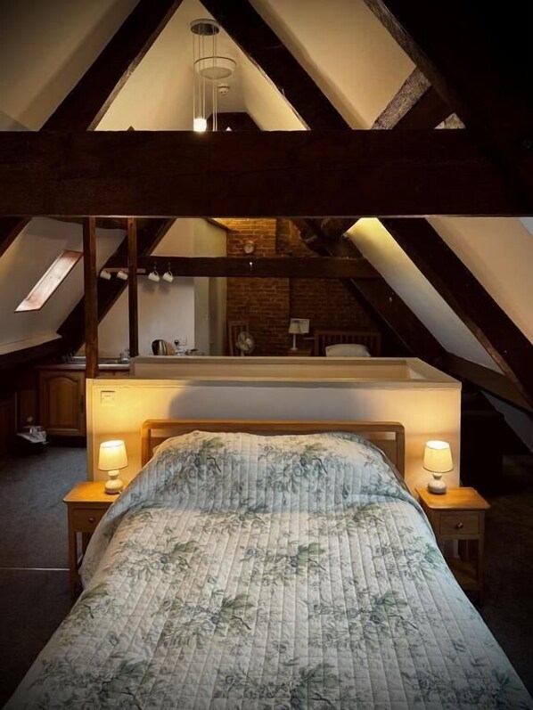 Un dormitorio en el ático con techo inclinado, una cama con ropa de cama floral, dos lámparas de noche y un espejo sobre la cama.