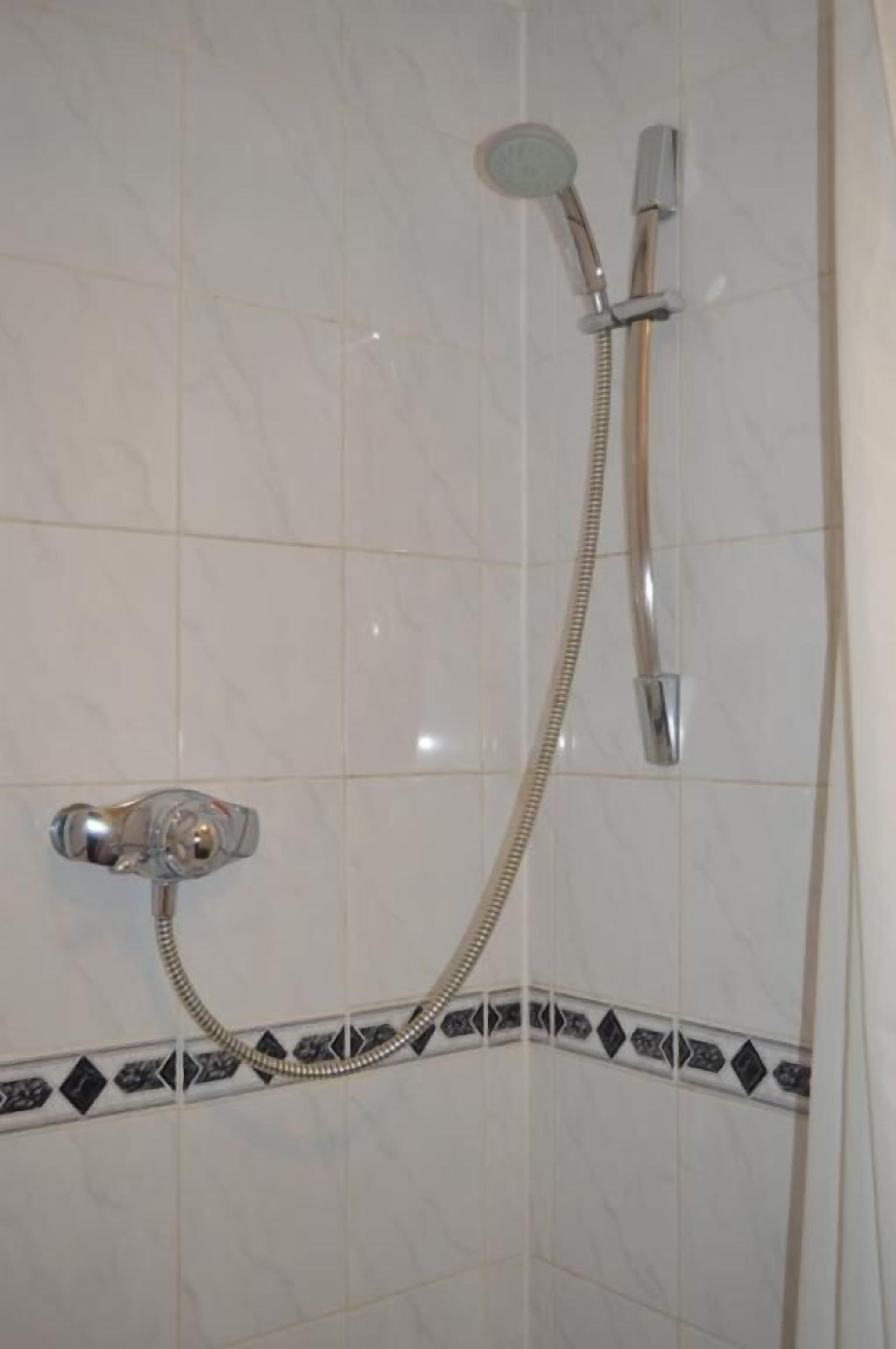 A shower with a handheld showerhead and a wall-mounted faucet.
