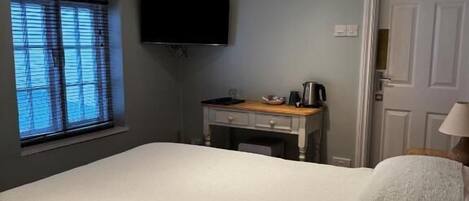 A bedroom with a bed, a desk, a television, and a door.