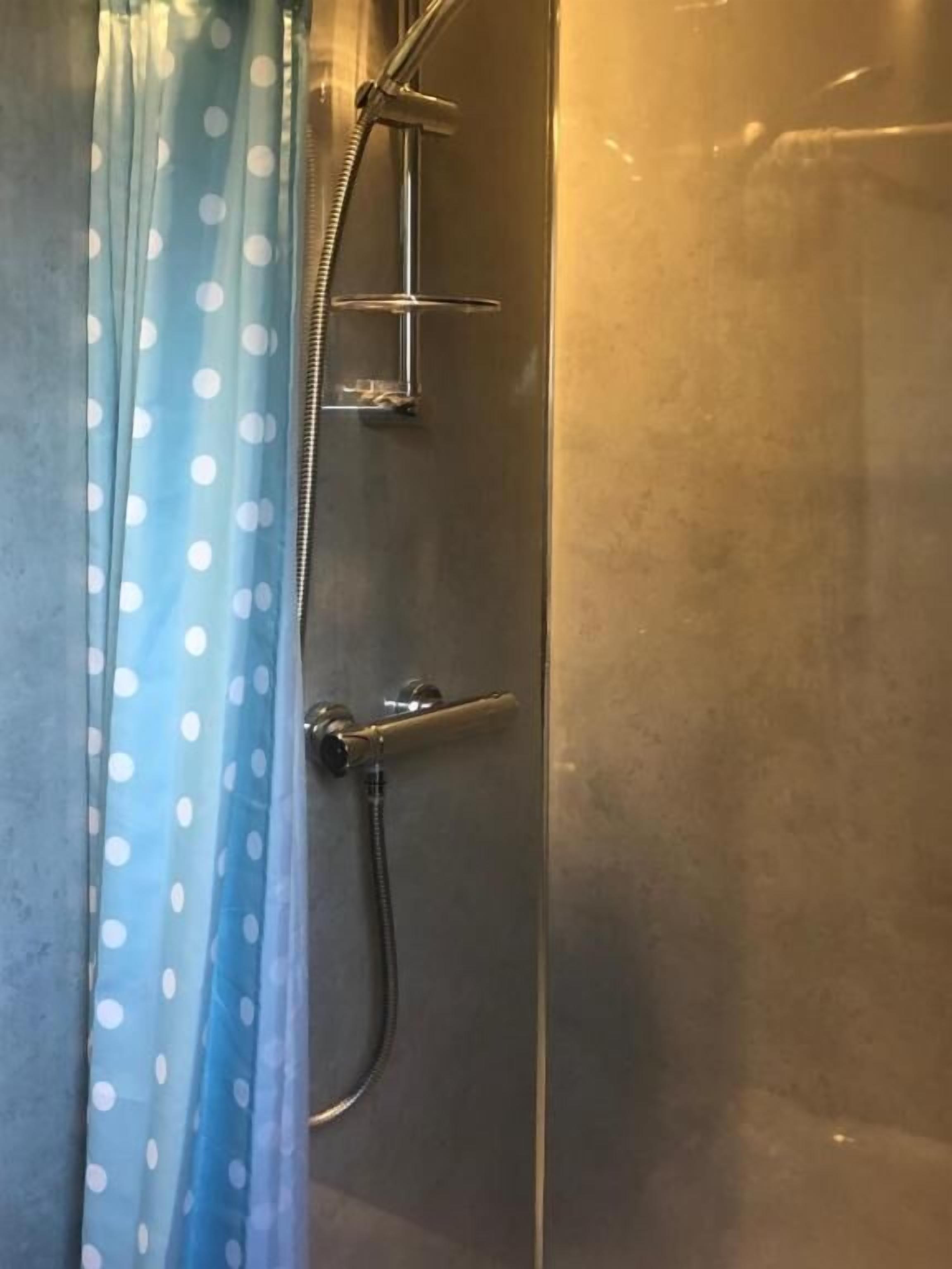 Ducha con cabezal de ducha manual, grifo de pared y cortina estampada con lunares.