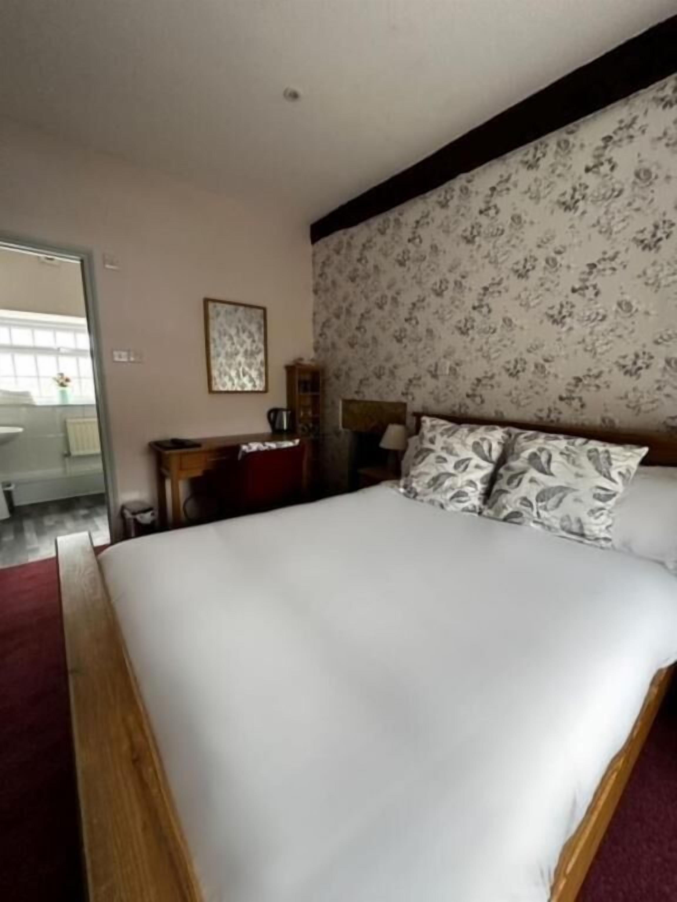 A hotel room with a large bed, a desk with a chair, a wooden headboard, a framed picture on the wall, and a window with a view.