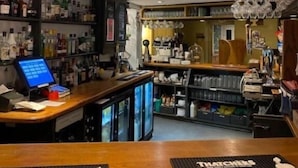 Een bar met een counter, planken met flessen en een displaykast.