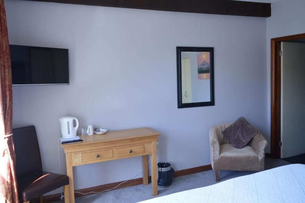 Une chambre comprenant un lit, un bureau avec une bouilloire, une chaise, une télévision et un tableau encadré au mur.