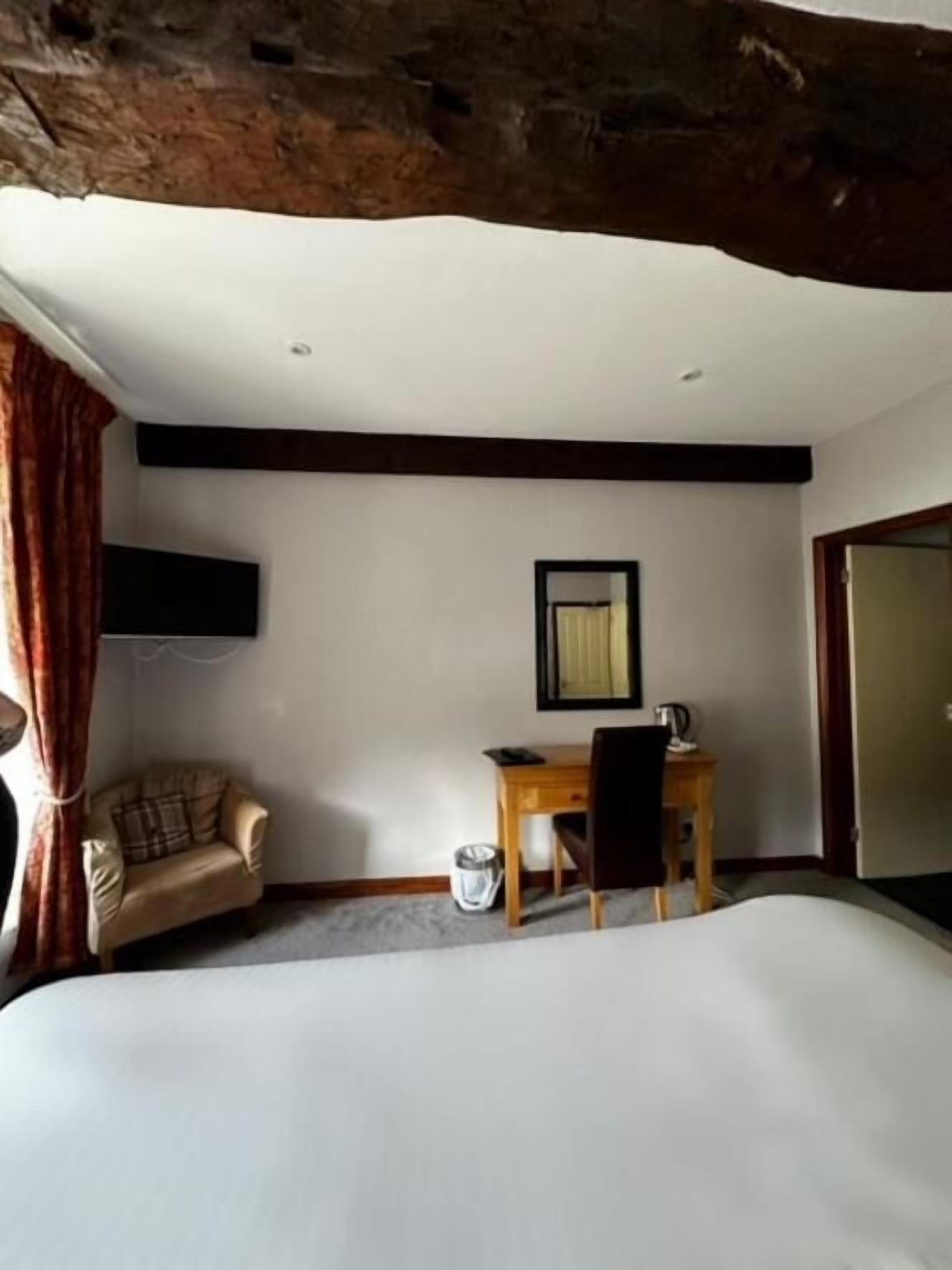 Ein Hotelzimmer mit Bett, Schreibtisch, Stuhl, Wandfernseher und einem fensterbepflanzten Fenster.