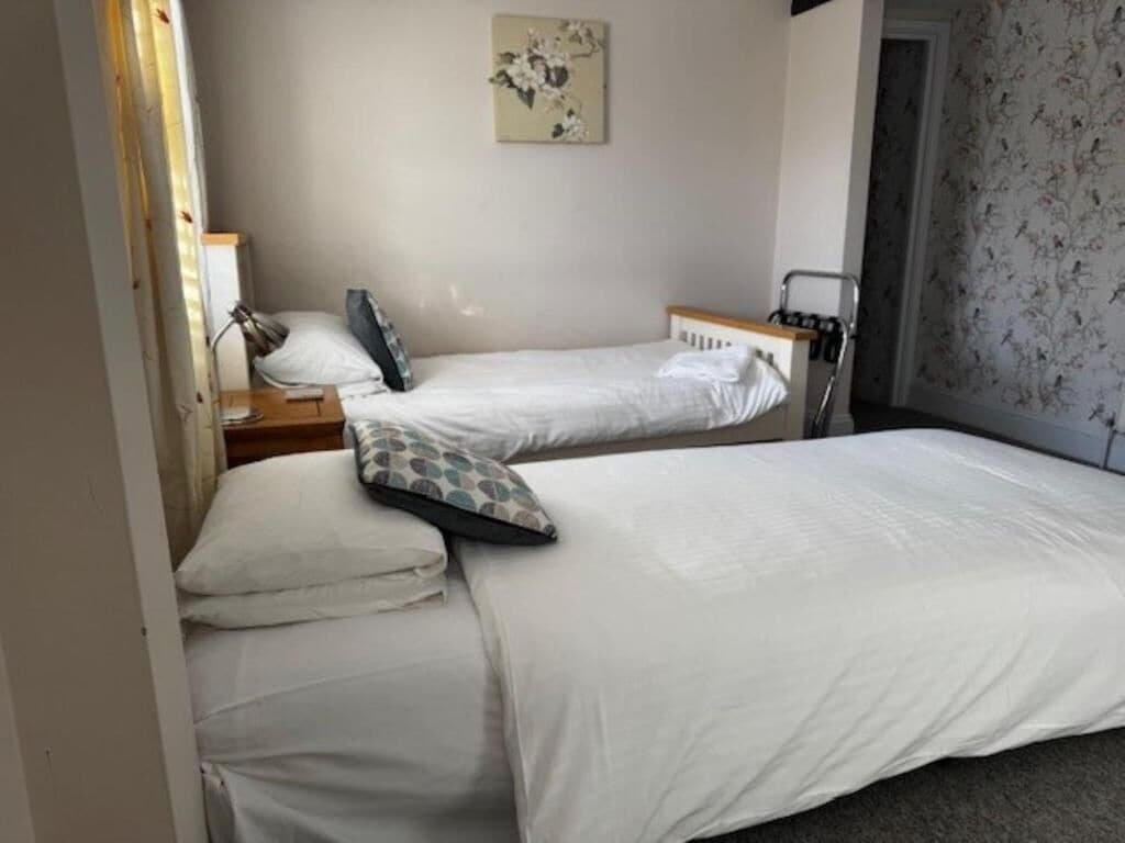 Una habitación de hotel con dos camas, una mesita de noche con lámpara, una obra de arte colgada en la pared y una puerta que da a otra habitación.
