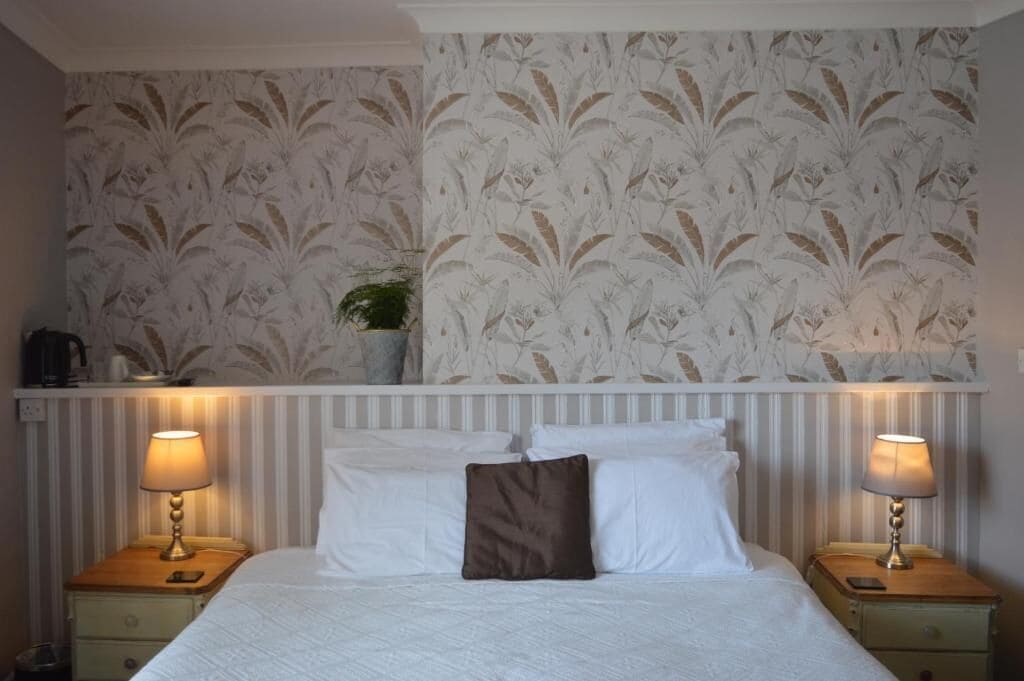 A hotel room with a bed, two bedside tables with lamps, a plant on the wall, and striped wallpaper.