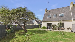 Una propiedad residencial con patio trasero cercado, un árbol y una casa con techo inclinado y ventanas.