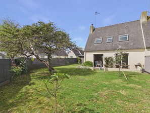 Ein Wohnhaus mit eingezäuntem Garten, einem Baum sowie einem Haus mit schrägem Dach und Fenstern.