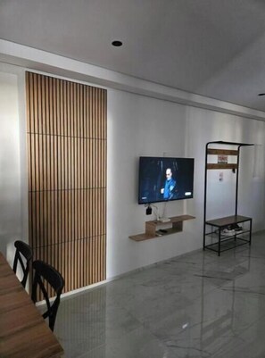 A modern room with a flat-screen TV mounted on the wall, a wooden slat partition, a metal shelf with a computer, and a metal chair. - Apartement s+2 haut standing a la soukra avec un parking privé (Tunis)