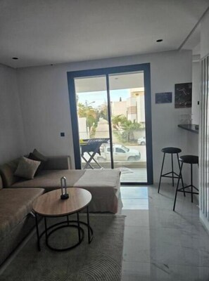 A modern living room with a sofa, a small round table, and a glass door leading to a balcony. - Apartement s+2 haut standing a la soukra avec un parking privé (Tunis)