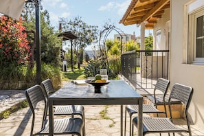 Un patio al aire libre con mesa y sillas, rodeado de plantas y vistas a un edificio.