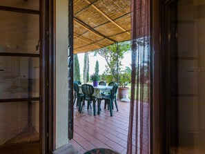 An open door leading to an outdoor patio with a table and chairs, surrounded by potted plants and trees. - Podere Tre Termini by Interhome (Cecina)