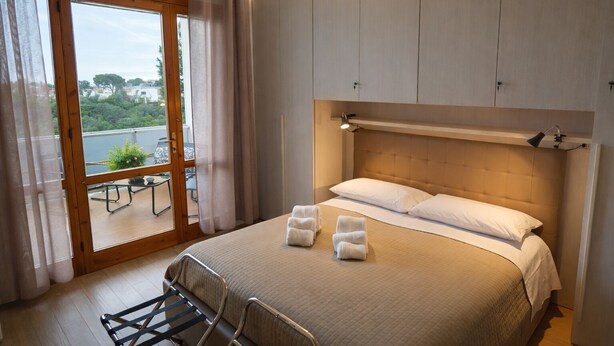 A bedroom with a large bed, a view through a sliding glass door, and a balcony with outdoor furniture. - Poggio delle Ginestre Vacation Home in Torre a Mare, Bari—Pool, Parking, Sleeps 4 (Parco Scizzo-parchitello)