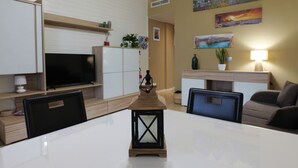 A modern living room with a flat-screen TV, a dining table, and a coffee table. There are decorative items on the shelves and a painting on the wall. - Poggio delle Ginestre Vacation Home in Torre a Mare, Bari—Pool, Parking, Sleeps 4 (Parco Scizzo-parchitello)