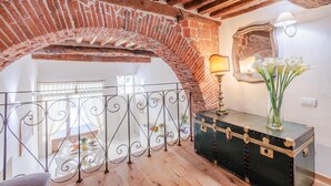 Una habitación con un arco de ladrillo, barandilla metálica, una mesa con vajilla y una maleta antigua.