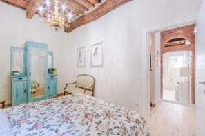 A bedroom with a floral bedspread, a blue wardrobe, a chair, and a chandelier. - Antica Tipografia in Lucca (Lucca)