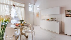 Una cocina moderna con armarios blancos, una estufa a gas y un lavabo. Hay una zona de comedor con una mesa redonda y sillas.