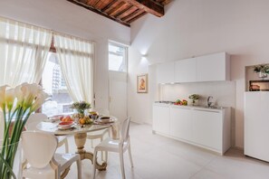 A modern kitchen with white cabinets, a gas stove, and a sink. There is a dining area with a round table and chairs. - Antica Tipografia in Lucca (Lucca)
