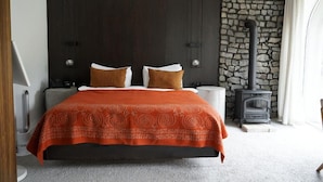 A bedroom with a bed, two nightstands, a stone wall, and a wood-burning stove. - Pana Unique Kolsay (Almaty)
