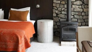 A bedroom with a bed, a stone wall, a fireplace, and a wooden door. - Pana Unique Kolsay (Almaty)