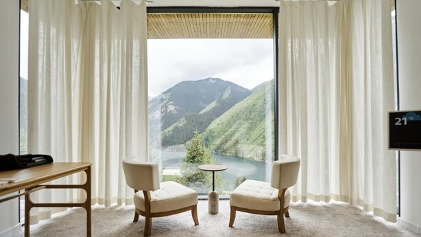 A room with a large window, two chairs, a small table, and a coat rack. - Pana Unique Kolsay (Almaty)