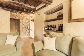 A cozy room with a stone wall, wooden beams, a sofa, and a wine rack. - 7BR Tuscan Oasis with Pool_Borgo sulla Visona (Capannori)
