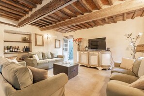 A living room with a sofa, a coffee table, a TV on a cabinet, and wine bottles on shelves. - 7BR Tuscan Oasis with Pool_Borgo sulla Visona (Capannori)