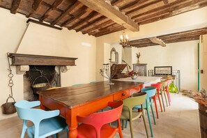 A rustic dining area with a wooden table, colorful chairs, a fireplace, and a chandelier.