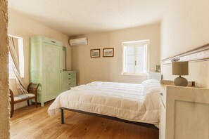 A bedroom with a bed, a dresser, a chair, an air conditioning unit, and a window.
