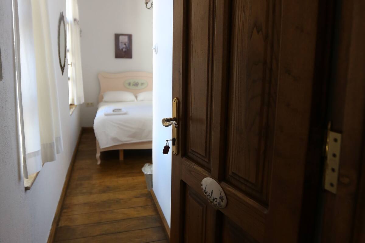 Un estrecho pasillo que conduce a un dormitorio con una puerta de madera, una cama y un cuadro colgado en la pared.