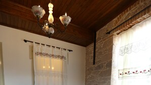 A double bed with a wooden headboard, a chandelier, a stone wall, and a window with a curtain. - Kidalyo Hotel (Ayvalik)