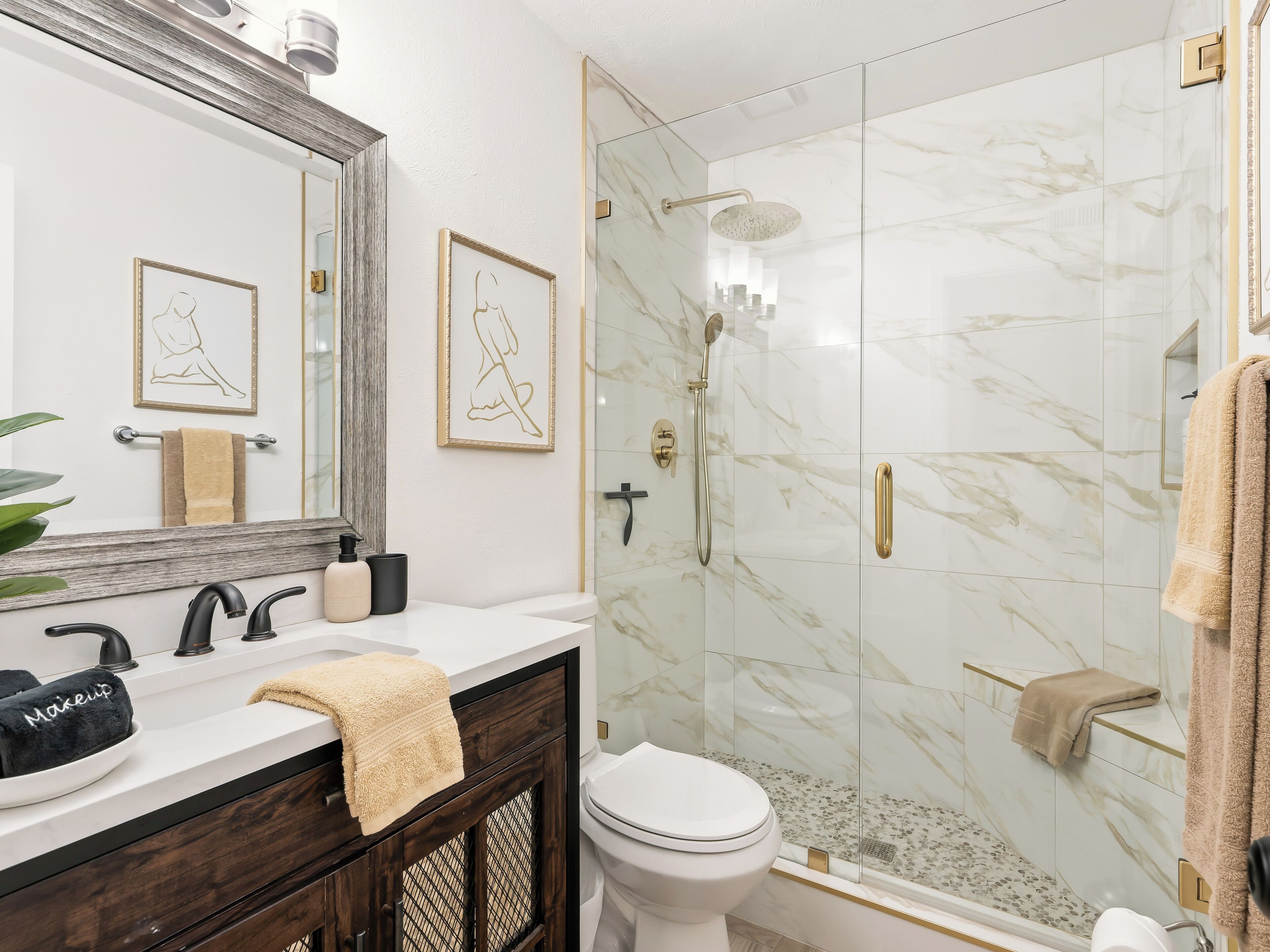 A bathroom with a shower, toilet, vanity, and a large mirror.