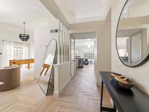 A modern interior with a herringbone floor, a wooden foosball table, a round mirror, and a dining area in the background.