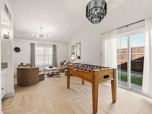 Amplia sala de estar con mesa de futbolín, sofá, mesa de centro y candelabro.