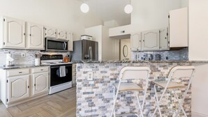 A modern kitchen with white cabinetry, a granite countertop, a built-in oven, a microwave, and a refrigerator. - Berrywood Stay / Pool + Fire Pit + Foosball (Garland)