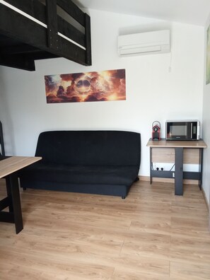 A room with a black sofa, a wooden dining table, a microwave, and an air conditioning unit. - Happy House (Valensole)